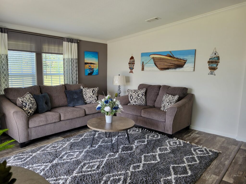 Interior of large manufactured, living room with two couces, rug, and beach wall decorations.